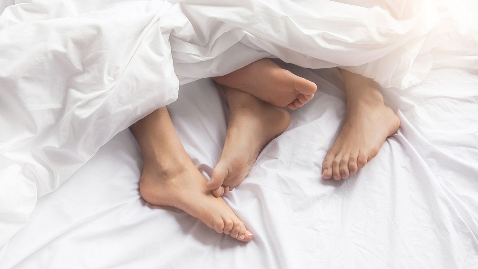 pies de dos personas en la cama con sábanas blancas