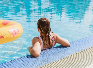 Mujer jóven en una piscina junto a un flotador amarillo vista de espaldas